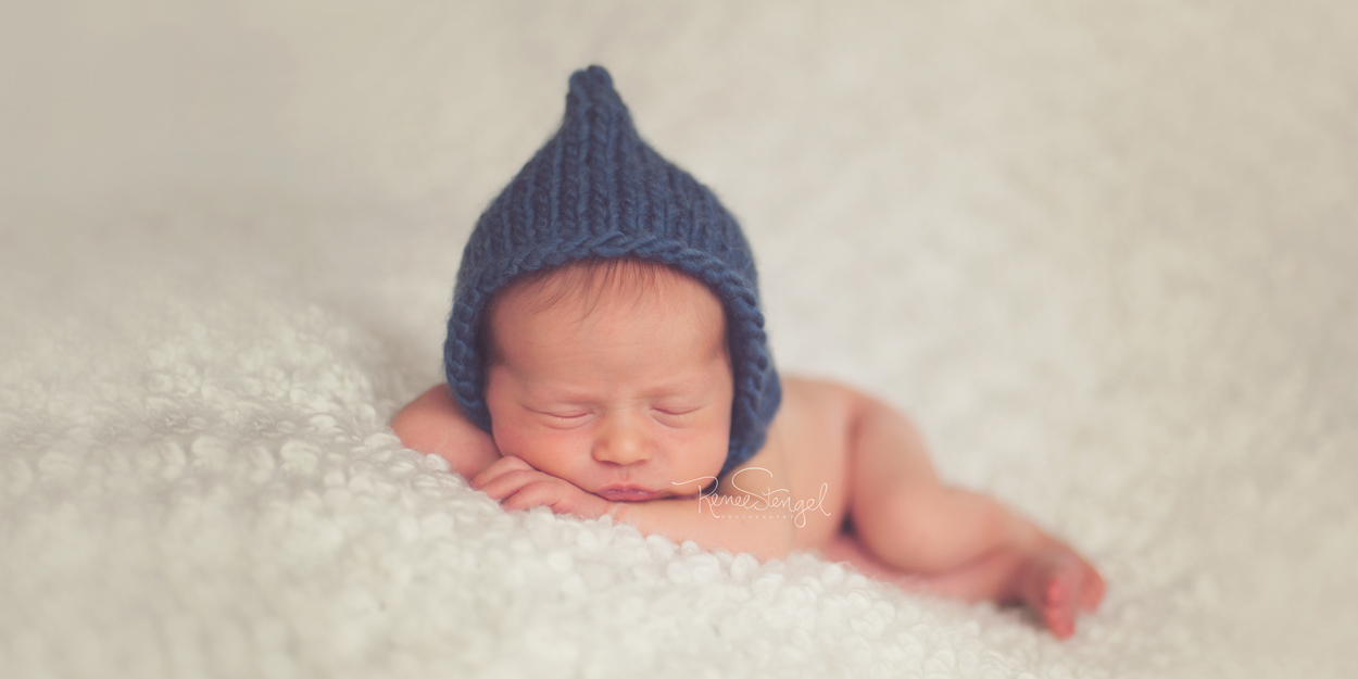Sleeping newborn photo with blue pixie bonnet on cream Ofelia blanket by IKEA