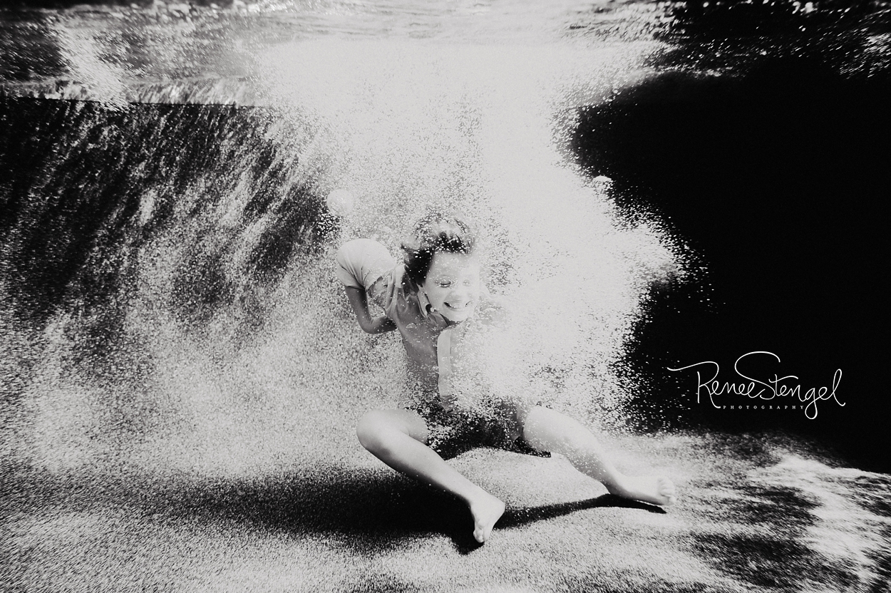 Black and White Underwater image of boy in holiday clothes as he jumps in.  The big Cannonball Boy in Bubbles