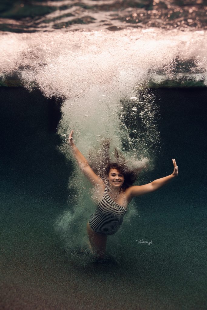 Underwater Senior Jumping In in a Striped Navy JCrew Swimsuit surrounded by lots of bubbles in a deep blue pool