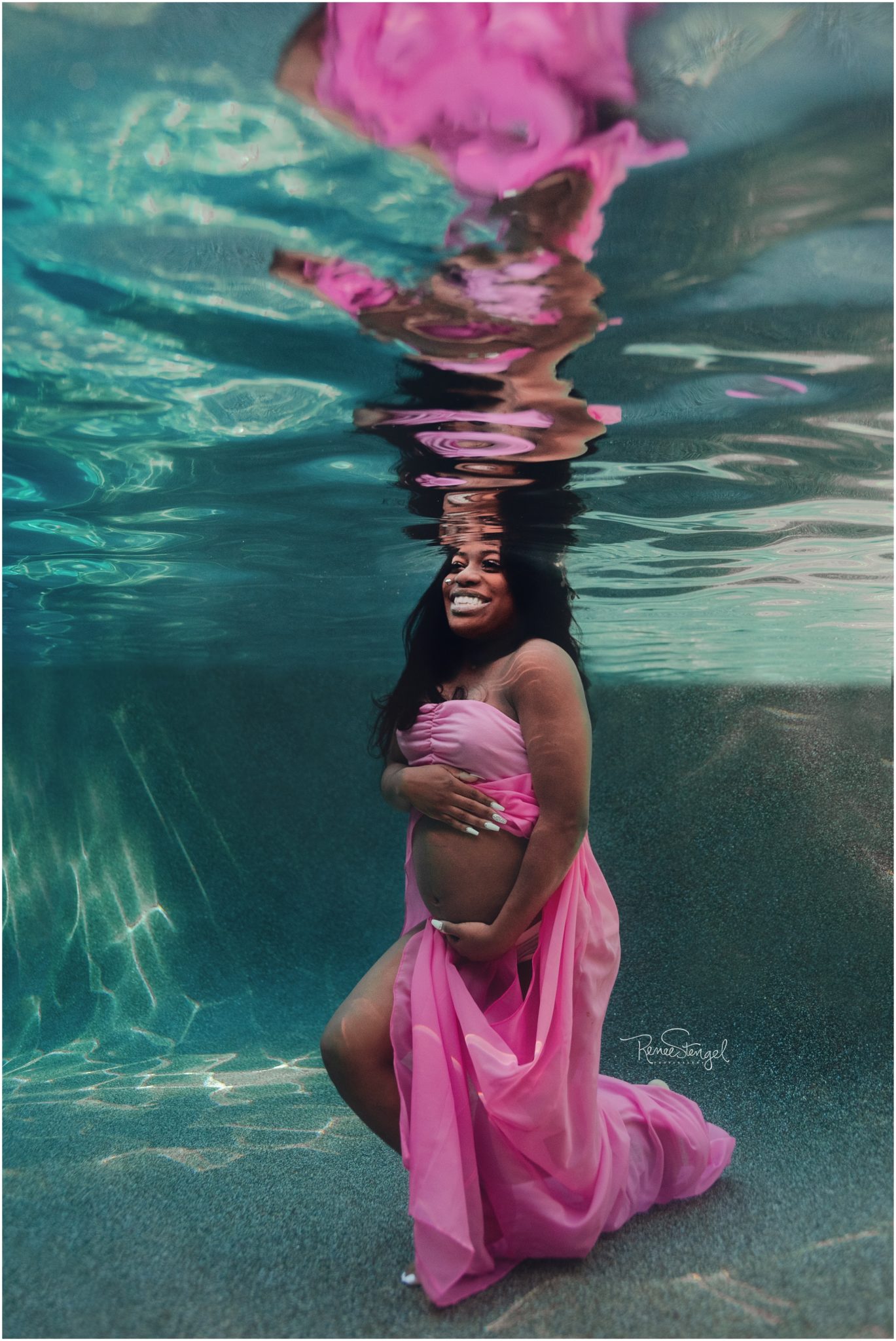 African American with big smile Underwater in pink open belly maternity gown