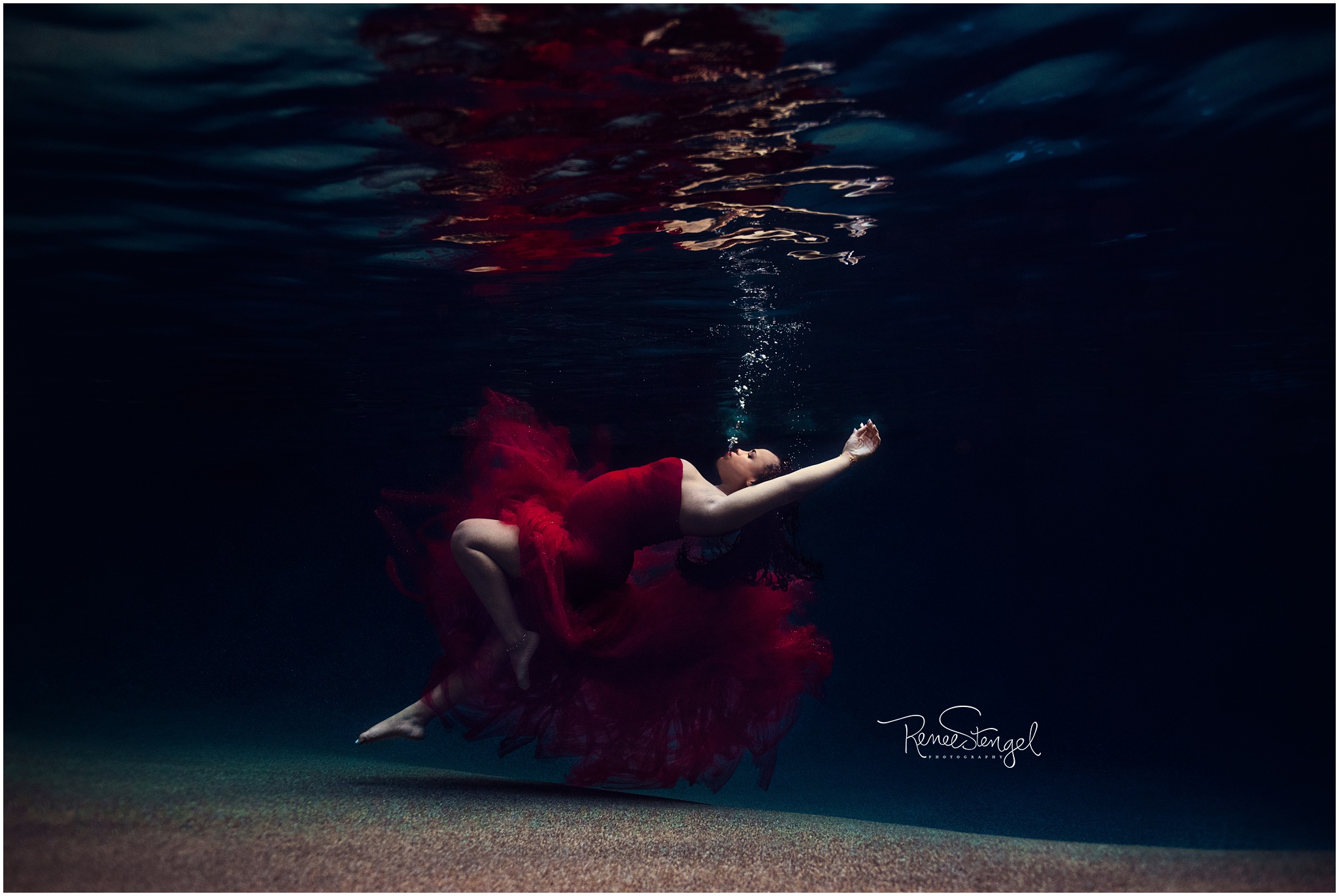 Unique Underwater Maternity Portrait of African American Woman in Red Tulle Couture Gown Sinking and blowing bubbles
