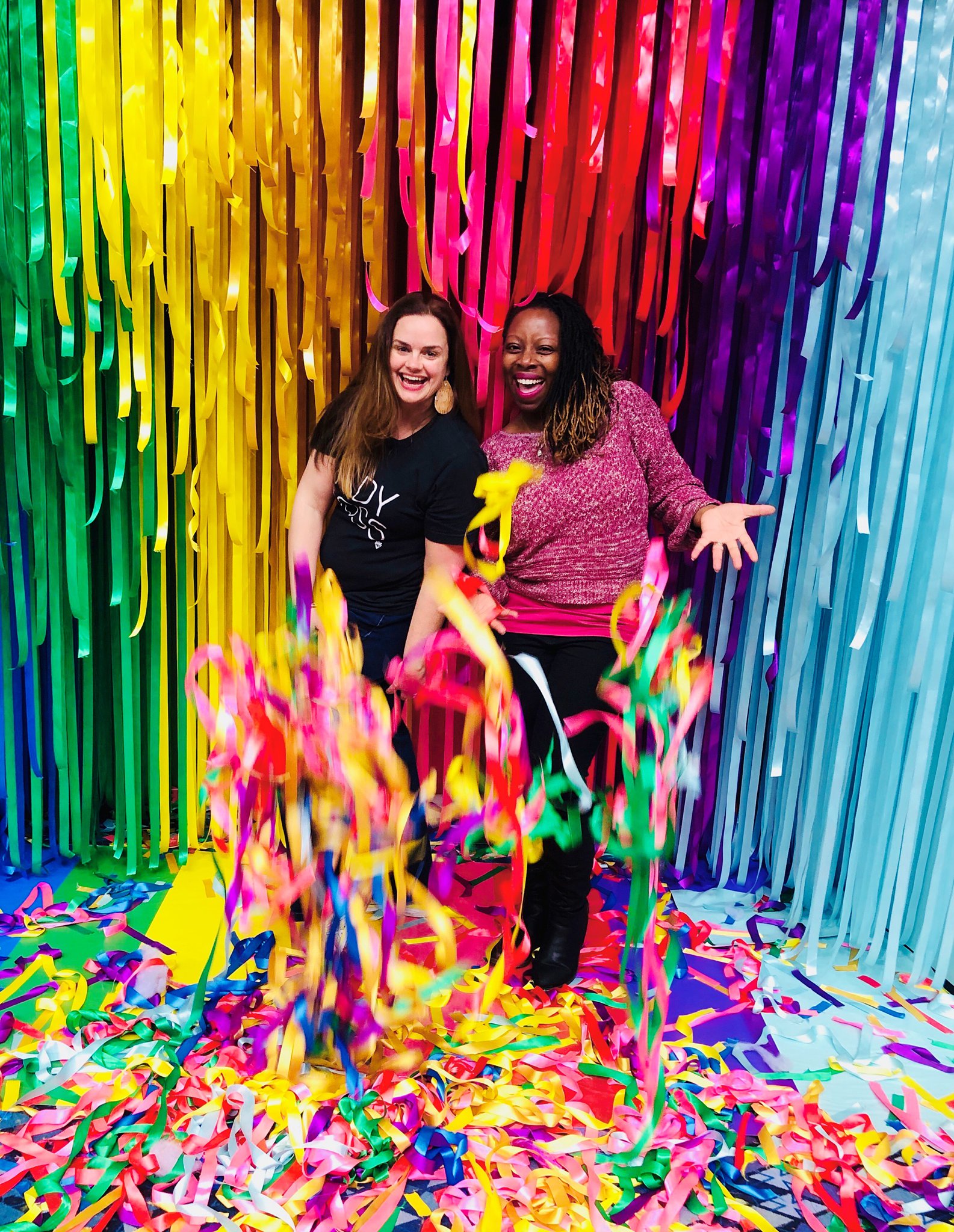 White and Black Female Photographers laughing in front of rainbow streamers at Imaging USA in Nashville Tennessee